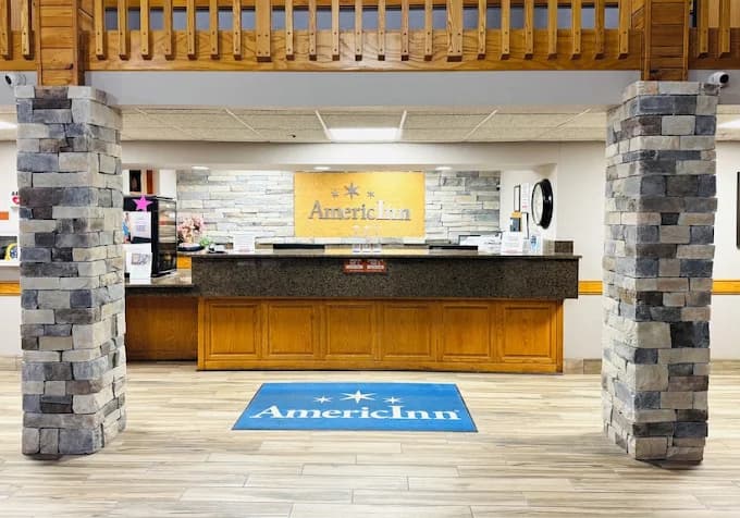 AmericInn hotel lobby featuring a granite reception desk, stone pillars, and branded floor mat.