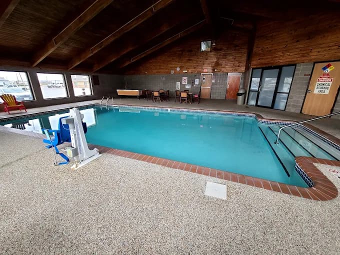 Indoor swimming pool featuring a wooden ceiling, accessible lift chair, and a seating area.