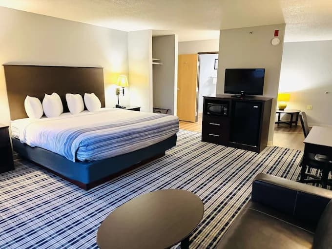 Spacious hotel room with a large bed, striped carpet, television, and small seating area.